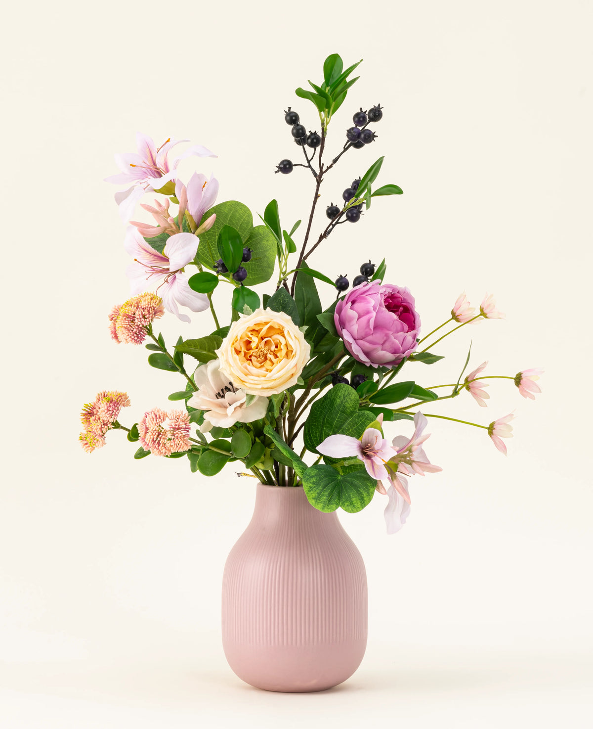 Het Zijden kunstbloemen boeket Touch of Cloudlight, gepresenteerd in een roze keramieken vaas, bevat roze pioenrozen, gele rozen, kleine bloesems, groen en takken met donkere bessen tegen een lichte achtergrond.