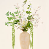 Een boeket van zijden kunstbloemen, Crystal Garden, bestaande uit witte en groene bloemen en hangend blad in een hoge, beige vaas met structuur.