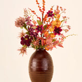 Zijden kunstbloemenboeket Amber Bloom, bestaande uit oranje, paarse en rode zijden bloemen in een bruine, geribbelde vaas.