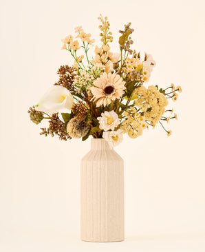Zijden kunstbloemenboeket Latte Macchiato met crèmekleurige, witte en bruine bloemen in een hoge, geribbelde, gebroken witte vaas.