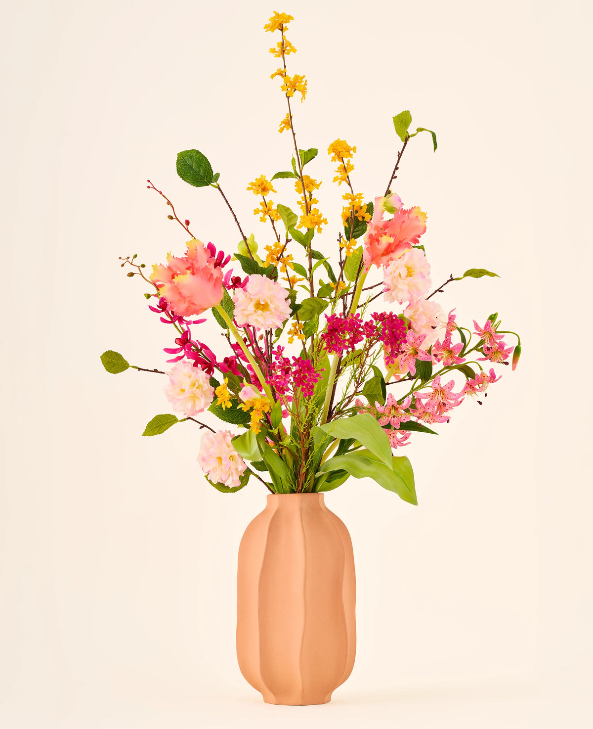 Zijden kunstbloemenboeket Spring Fling met gele forsythia, roze tulpen en kleine roze bloesems in een perzikkleurige geribbelde vaas.