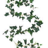 De Kunst hangplant Klimop Boston Slinger 180 cm groen heeft een enkele kunstmatige klimoprank met donkergroene bladeren die elegant kronkelt op een witte achtergrond.