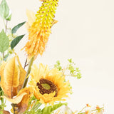 Het Zijden kunstbloemen boeket Amber Light heeft een gele zonnebloem, een lange geeloranje stekelige bloem, groene bladeren en kleine witte bloemen tegen een lichtcrème achtergrond met een amberkleurige gloed.