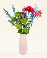 Het Zijden kunstbloemen boeket Blossom Breeze heeft roze, blauwe, groene en paarse bloemen in een roze keramische vaas - perfect om een levendig accent aan elke kamer te geven.