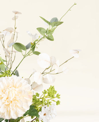 Een close-up van het Zijden kunstbloemen boeket Claire de Lune, met witte en crèmekleurige bloemen, groene bladeren en delicaat wit gebladerte op een lichte, neutrale achtergrond.