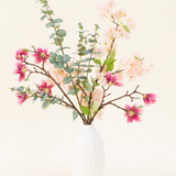 In een vaas met witte structuur staat het Zijden kunstbloemen boeket Featherlight Florals met zachtroze en diepmagenta zijden bloemen, plus groene eucalyptusbladeren op lange stelen, tegen een lichte achtergrond.
