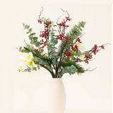 Het Zijden kunstbloemen boeket Midwinter Dream heeft groene bladeren, dennentakken, rode bessen en witte bloemen in een vaas met witte structuur - perfect voor een sereen winterboeket tegen een effen lichte achtergrond.
