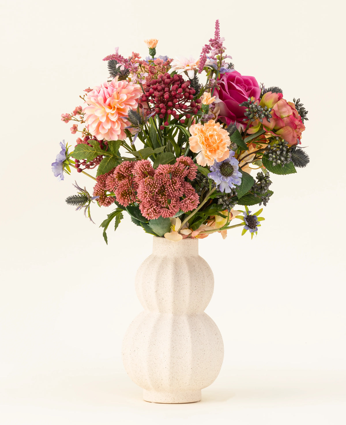 In een witte, gebogen vaas van keramiek staat het Zijden kunstbloemen boeket Pretty Pastel - een kleurrijke mix van duurzame bloemen zoals roze rozen, dahlia's, paarse en oranje bloemen en groen - prachtig gerangschikt tegen een lichte achtergrond.