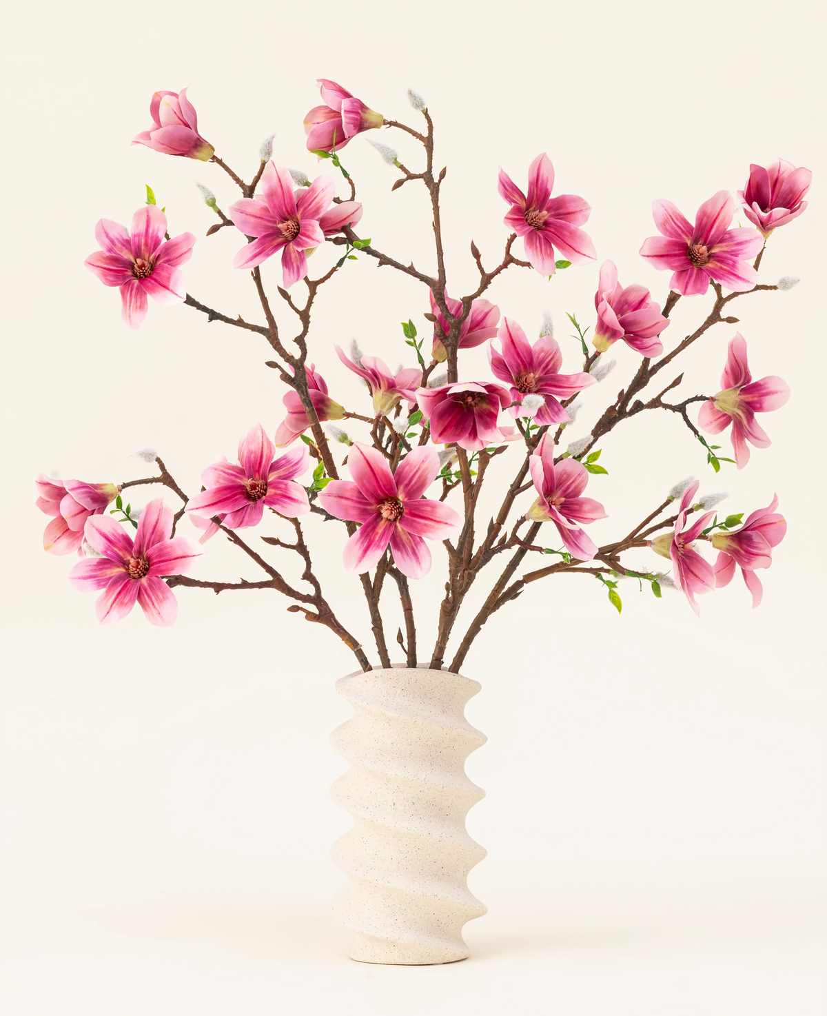 De Zijden kunstbloemen boeket Magnolia roze is gerangschikt in een golvende vaas van wit keramiek met groene knoppen, waardoor een elegante display ontstaat tegen een lichte achtergrond.