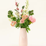 Een roze vaas van keramiek toont het Zijden kunstbloemen boeket Daisy Charm, met verschillende bloemen en groen - roze rozen, witte bloesems en rode bessen - prachtig gerangschikt tegen een effen lichte achtergrond.
