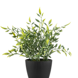 Een Kunstplant Bamboe 28 cm, een bladgroene potplant met lange, slanke bladeren, sommige met een gele punt, groeit in een verticaal geribbelde zwarte pot tegen een effen witte achtergrond.