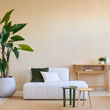Een minimalistische woonkamer met de Kunstplant Calocasia 210 cm, een bank met witte textuur en groene en witte kussens, twee kleine bijzettafeltjes, een beige vloerkleed en een houten consoletafel tegen een lichtbeige muur.