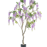 De Kunstplant Blauweregen 180 cm heeft een gedraaide stam met levensechte trossen paarse bloemen en groene bladeren tegen een witte achtergrond.