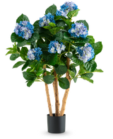 De Kunstplant Hortensia 85 cm blauw is een kunstplant in pot met hoge houten stelen en weelderige groene bladeren, met meerdere trossen blauwe en lichtpaarse hortensiabloemen in een eenvoudige zwarte pot.