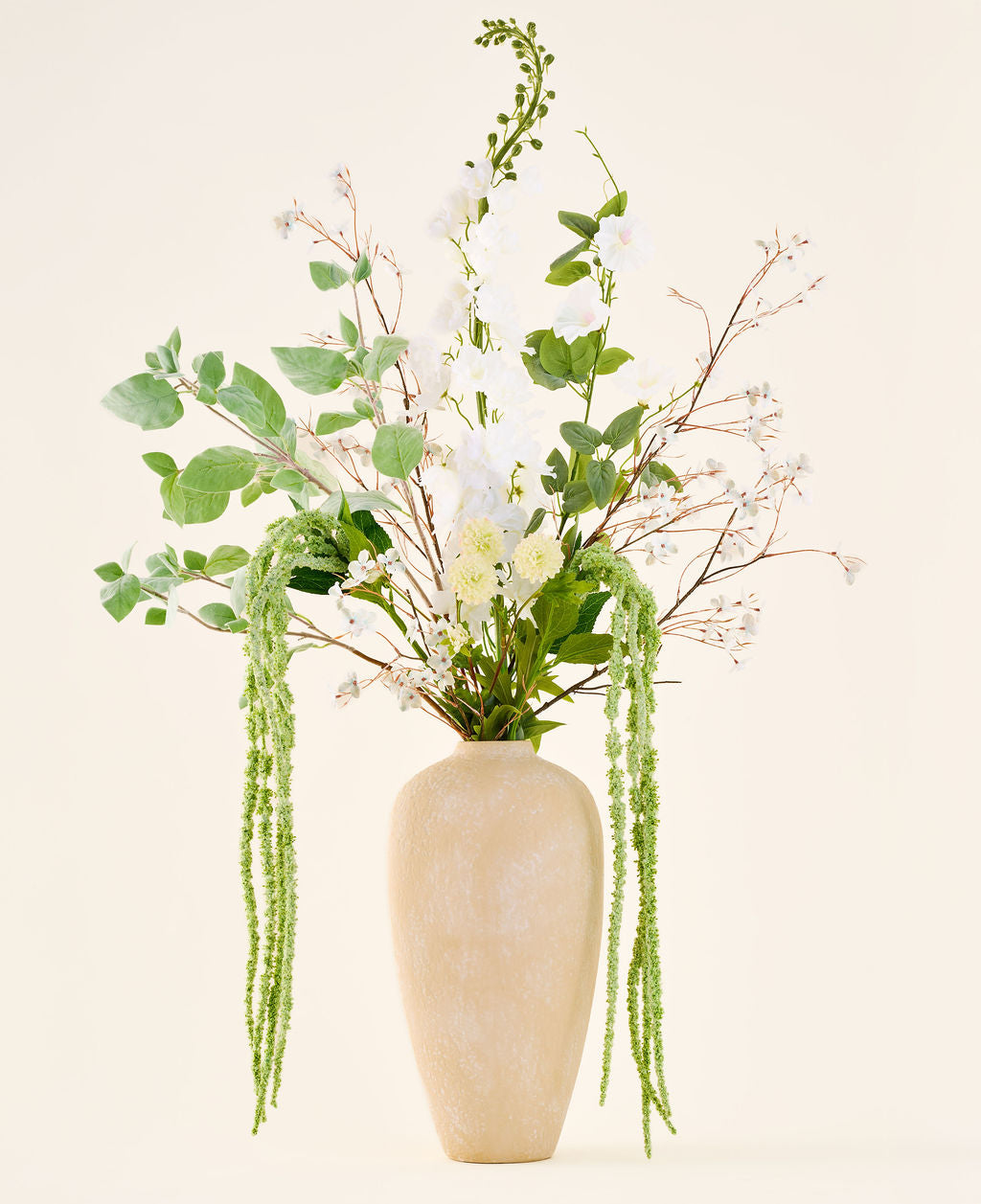 Een boeket van zijden kunstbloemen, Crystal Garden, bestaande uit witte en groene bloemen en hangend blad in een hoge, beige vaas met structuur.