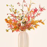 Zijden kunstbloemenboeket ‘Autumn Breeze’ in een witte keramische vaas, met een arrangement van herfstbladeren, kleine groene besjes, roze bloemen en witte bloemen, vervaardigd uit hoogwaardige zijden bloemen. Geplaatst tegen een lichte achtergrond – het perfecte kunstbloemenboeket om elke ruimte langdurig een seizoenssfeer te geven.