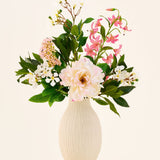 In een crèmekleurige keramische vaas staat het boeket ‘Light & Lovely’ met zijden kunstbloemen van Easyplants, bestaande uit een gemengd arrangement van witte, roze en lichtpaarse zijden bloemen met groene bladeren, tegen een effen, lichte achtergrond.