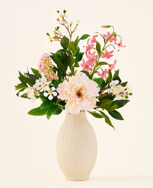 In een crèmekleurige keramische vaas staat het boeket ‘Light & Lovely’ met zijden kunstbloemen van Easyplants, bestaande uit een gemengd arrangement van witte, roze en lichtpaarse zijden bloemen met groene bladeren, tegen een effen, lichte achtergrond.