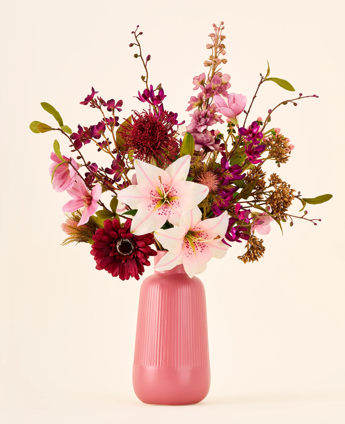 Een boeket van roze, bordeauxrode en witte Zijden kunstbloemen, het boeket Burgundy Dream, in een geribbelde roze vaas.