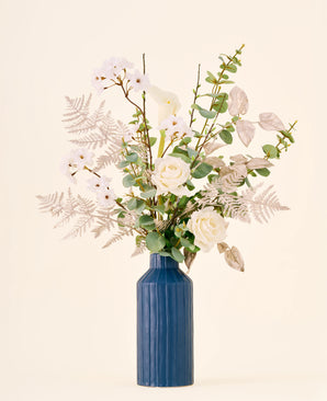 Zijden kunstbloemenboeket Silent Night, bestaande uit witte rozen en calla’s in een hoge, geribbelde blauwe vaas.
