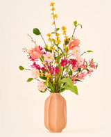 Zijden kunstbloemenboeket Spring Fling met gele forsythia, roze tulpen en kleine roze bloesems in een perzikkleurige geribbelde vaas.