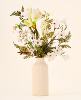 Een boeket van Zijden kunstbloemen, Winter Forest, met witte bloemen en groen in een geribbelde, gebroken witte keramische vaas.
