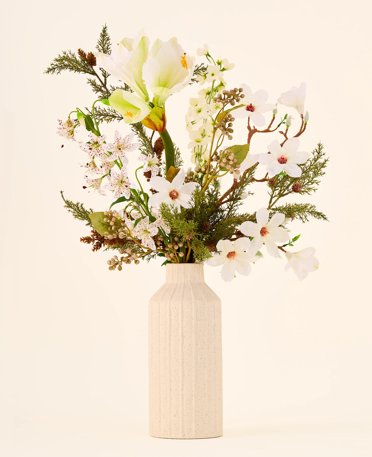Een boeket van Zijden kunstbloemen, Winter Forest, met witte bloemen en groen in een geribbelde, gebroken witte keramische vaas.