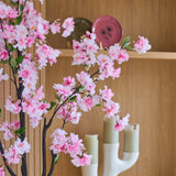 De ‘Kunst Kersenbloesem’ (150 cm) met roze takken is voor houten planken geplaatst, waarop groene kaarsen in een witte kandelaar en decoratieve borden staan uitgestald.