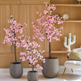 Drie Kunstplant-bougainvilles van 180 cm, roze van kleur en met roze bloemen, staan voor houten wandplanken, naast een moderne witte stoel met een kussen.