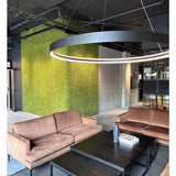 Een moderne zithoek met beige banken, zwarte salontafels, een grote ronde plafondlamp en op de achtergrond een groene muur, gecreëerd met Kunsthaag Nordic Mos 50x50 cm UV, die een luxe interieur en een eigentijds industrieel ontwerp uitstraalt.
