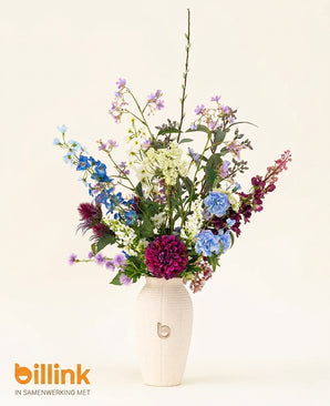 Een witte vaas met de letter b bevat het Zijden kunstbloemen boeket Purple Rain, met blauwe, paarse en witte bloemen. Op de effen lichte achtergrond staat linksonder het logo van billink, met Nederlands vakmanschap.
