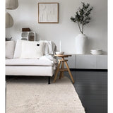Een minimalistische woonkamer met een lichtgekleurde bank, neutraal vloerkleed, wit dressoir, Kunst Olijfboom 120 cm als decoratief element, abstracte muurkunst en houten krukjes-alles in zachte Mediterrane sfeer met neutrale tinten.