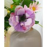 Een close-up van de Kunstanemoon Real Touch paars 52cm anemoon bloem in een mat witte vaas, omringd door groene bladeren en pastelkleurige bloemen.