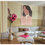 Een gezellige woonkamer met een lichtgrijs bankstel, roze en gouden accenten, een Kunstbloem Anemoon vertakt 56 cm roze in een moderne vaas, een salontafel met een bonten kleed en pastel abstracte kunst van een vrouw aan de muur.