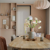 Een moderne eetkamer met een lichthouten tafel, vier stoelen met kussens, de Kunstbloem Fritillary 94 cm wit in een vaas, keramische kopjes, pastelroze muren, ingebouwde planken met decor en een grote ronde hanglamp boven je hoofd.