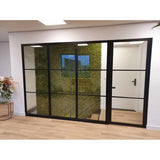 Een modern luxe interieur met een zwarte glazen wand onthult een groene wand van Kunsthaag Nordic Mos 50x50 cm UV, een trap erachter, lichte houten vloeren en een stijlvol bloemstuk aan de linkerkant.