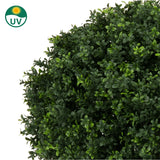 Close-up van Kunstplant Buxus op stam romeinse stijl UV 85cm, een ronde kunst buxusstruik met dichte, kleine groene bladeren. In de linkerbovenhoek staat een UV-beschermingssymbool met een zonne-icoon.
