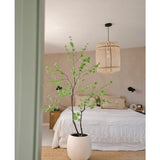 Een minimalistische slaapkamer met beige muren, een wit bed, een natuurlijk geweven tapijt en de Kunstplant Enkianthus 210 cm - een grote potplant met groene bladeren - op de voorgrond. Aan het plafond hangt een geweven hanglamp.
