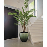 De Kunstplant Hawaii Parlour 180 cm, een hoge indoor kunstpalm met weelderige groene bladeren, staat op een grijze vloer in een moderne hal in de buurt van een witte trap en zwarte deur.
