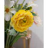 Een close-up van de Kunstranonkel Real Touch Geel 60cm, een levendige gele kunstranonkel met gelaagde bloemblaadjes, geschikt in een vaas binnenshuis naast witte en lichtroze bloemen.