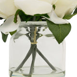 Een close-up van de Kunstrozenboeket Real Touch Wit 18cm: witte kunstbloemen met groene bladeren in een heldere glazen pot, zichtbare stelen bijeengehouden door een elastiekje.