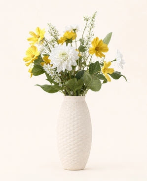 Zijden kunstbloemen boeket Sunny Whisper, een elegant boeket van gele en witte zijden bloemen met groene bladeren, gepresenteerd in een witte vaas tegen een lichte achtergrond.