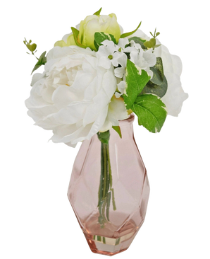 Het Kunstboeket in glas 25 cm heeft witte en lichtgroene kunstbloemen met groene bladeren in een roze geometrische glazen vaas, tegen een witte achtergrond.